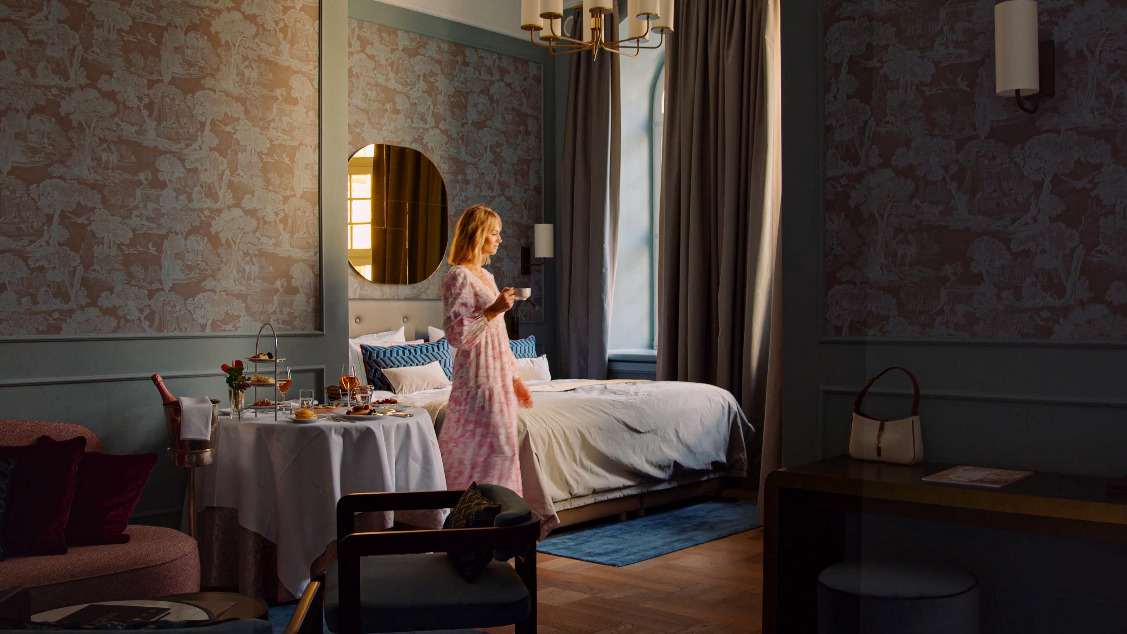 Moody Taschenbergpalais Kempinski Dresden room with lavish breakfast, large bed and woman walking towards window light.